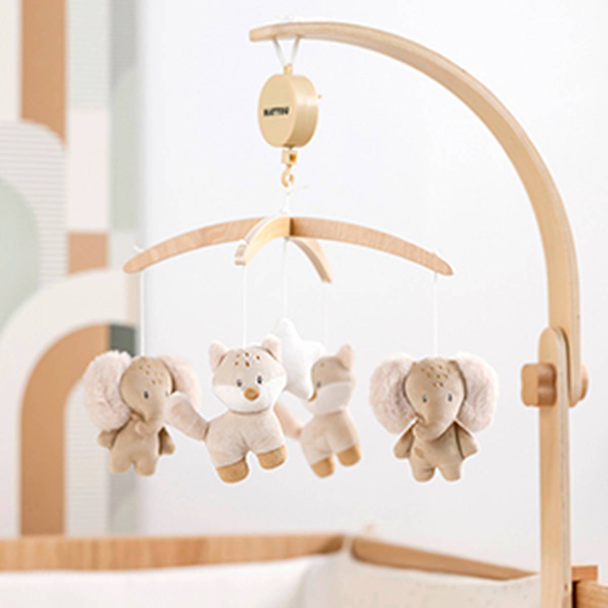 Ein hölzernes Babymobile mit Plüschfiguren – einem Elefanten und einem Fuchs –, das über einem Kinderbett hängt; Szene in einem sanft dekorierten Kinderzimmer.