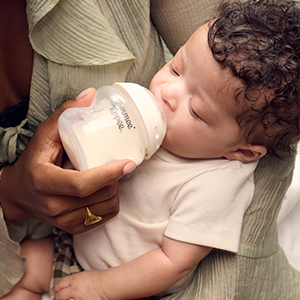 Baby wird mit einer Babyflasche gefüttert und liegt dabei auf dem Arm einer erwachsenen Person. Die Trinkflasche von Tommee Tippee unterstützt eine altersgerechte Nahrungsaufnahme.