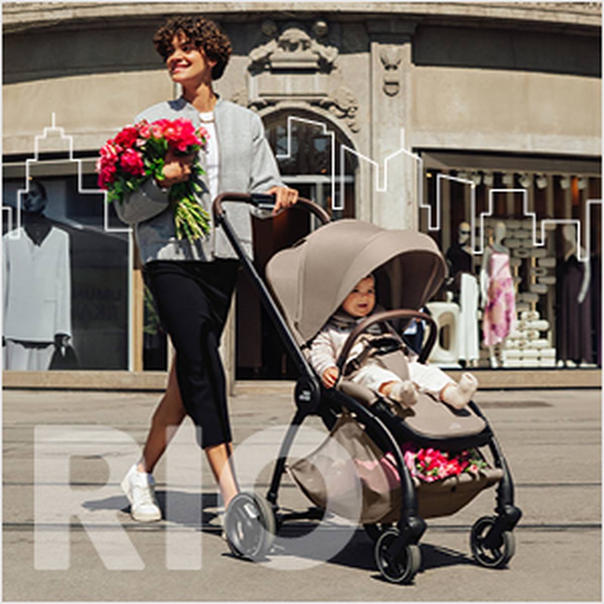 Eine Frau schiebt einen Kinderwagen mit einem Kind darin, hält einen Blumenstrauß in der Hand und geht fröhlich eine Straße in der Stadt entlang, im Hintergrund sind Schaufenster zu sehen.