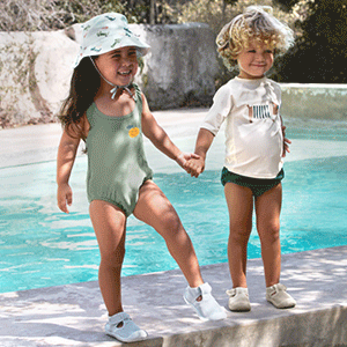 Zwei Kleinkinder spielen in ihrer bunten Bademode am Wasser.