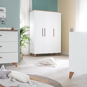 Ein modernes Kinderzimmer mit weißen Möbeln, darunter ein Kleiderschrank, eine Kommode und ein Babybett. Sanfte Beleuchtung und Pflanzen verleihen dem Raum eine gemütliche Note.