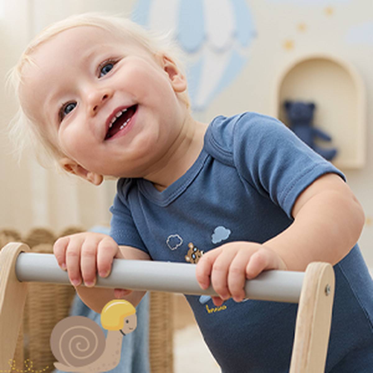 Ein lächelndes Baby in einem blauen Strampler lehnt an einem Holzgeländer in einem gemütlichen Zimmer mit sanften Farben und einem kleinen Stofftier im Hintergrund.