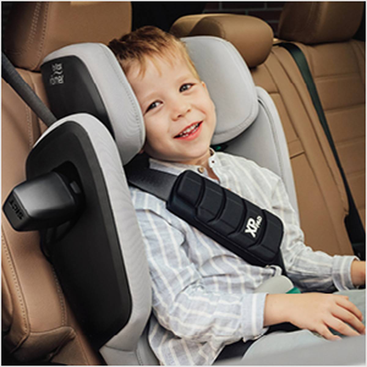 Lächelndes Kind in einem Britax Römer Autositz, gestreiftes Hemd, mit einem Sicherheitsgurt über der Brust befestigt.