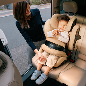 Kind sitzt angeschnallt in einem beige-farbenen Autokindersitz auf der Rückbank eines Fahrzeugs. Der Kindersitz verfügt über einen integrierten Seitenaufprallschutz und ein großer Bremsschutz unter dem Gurt.