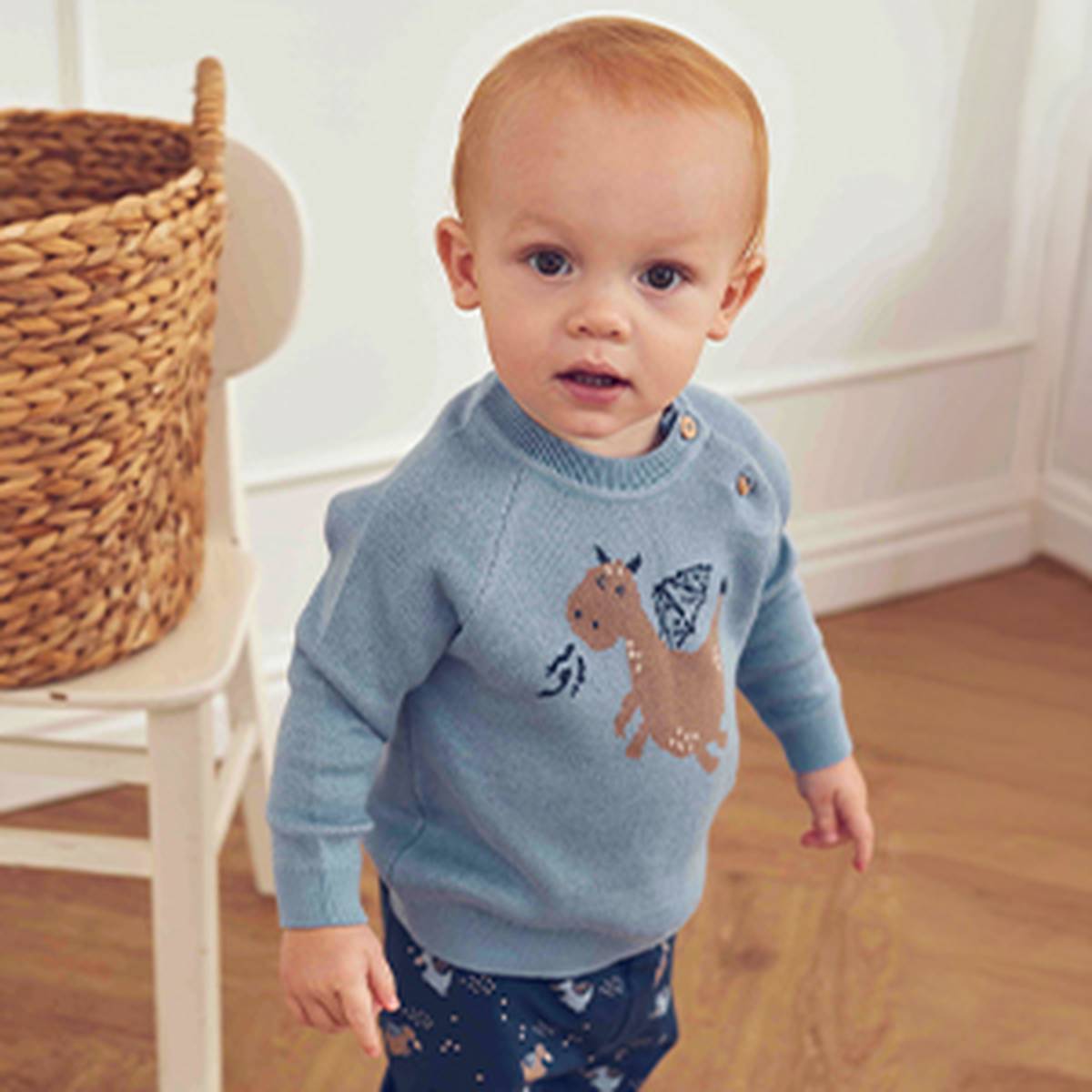 Kleinkind im hellblauen Strickpullover mit Pferde-Motiv und gemusterter Hose von muesli in wohnlicher Umgebung.