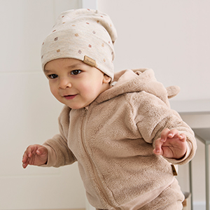 Kleinkind trägt eine helle Mütze und einen kuscheligen Zweiteiler mit Kapuze in Beige. Das weiche Outfit eignet sich für angenehmen Tragekomfort im Alltag.