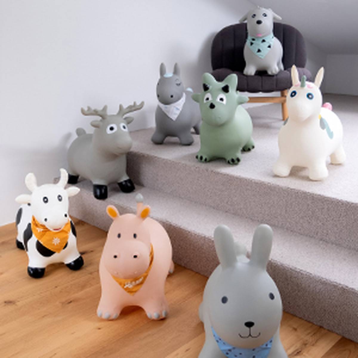 Seven inflatable animal toys with bandanas, including a deer, unicorn, cow, and rabbit, are arranged on a carpeted staircase and floor.