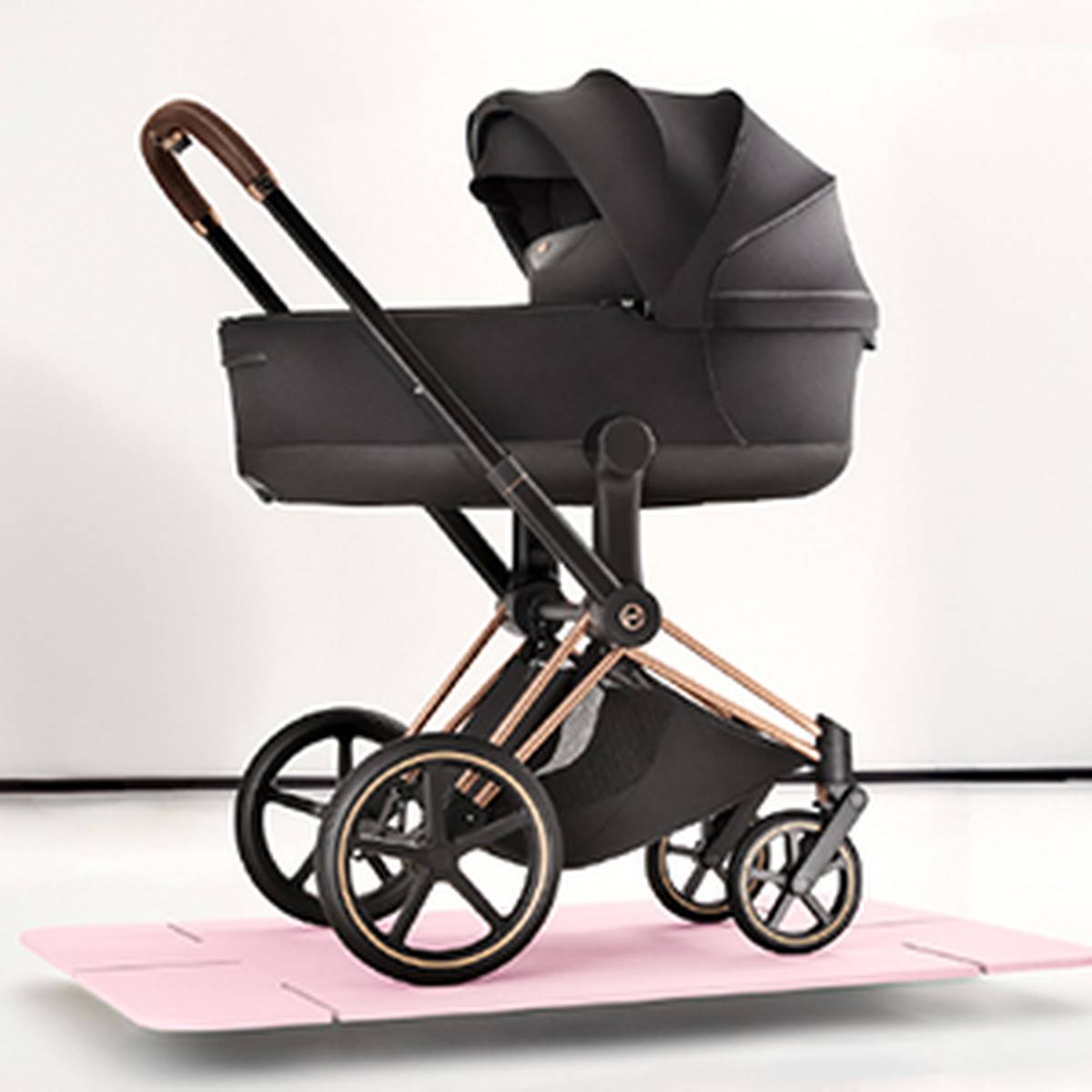 Ein eleganter, moderner schwarzer Kinderwagen mit roségoldenen Akzenten und großen Rädern, vor einem weißen Hintergrund mit einer rosafarbenen Bodenmatte.