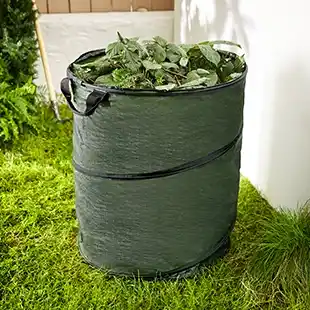 Eine grüne Pop-up-Gartentasche, gefüllt mit Laub, auf einer Rasenfläche in der Nähe einer Gartenmauer.
