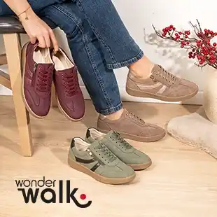 Eine Person sitzt auf einem Stuhl und probiert Freizeitschuhe in den Farben Bordeauxrot, Beige und Grün an; daneben steht eine Topfpflanze. Das „Wonder Walk“-Logo ist zu sehen.