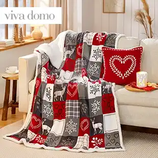 Wohndecke in Rot, Grau und Weiß mit Herz-, Hirsch- und Schneeflockenmotiven, dekorativ über Sofa und Sitzkissen in einem Wohnraum drapiert.