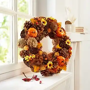 Ein Herbstkranz mit Tannenzapfen, kleinen Kürbissen und gelben Blumen, der auf einer Fensterbank liegt und in warmen Farbtönen gestaltet ist.