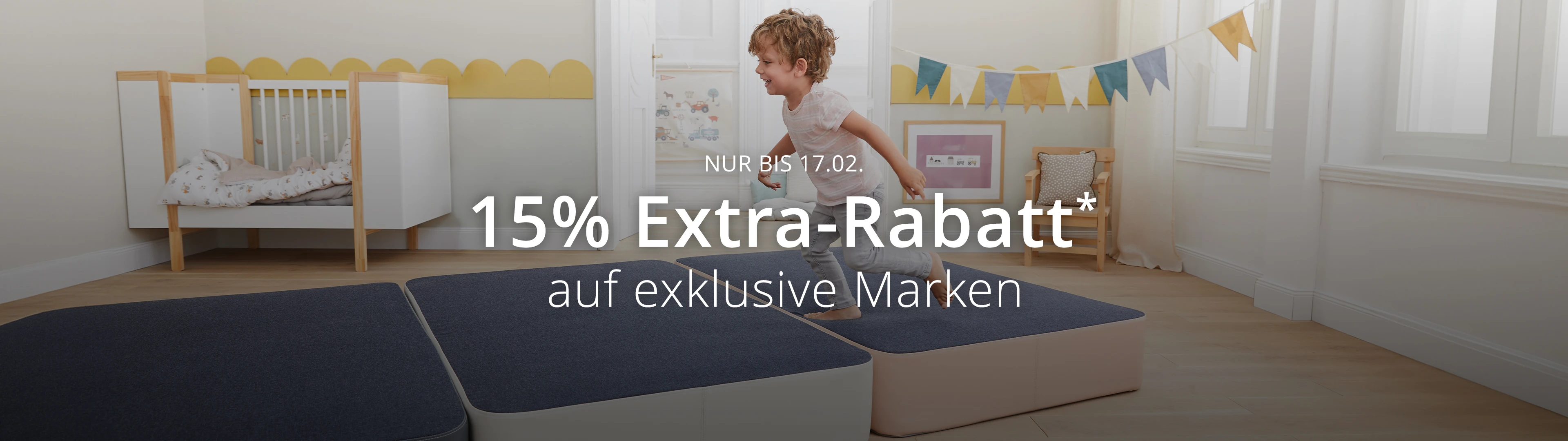 Ein Kind hüpft vergnügt auf einer blauen Matte in einem mit Kunst und einem Banner dekorierten Zimmer. Der Text bietet 15 % Extra-Rabatt* auf exklusive Marken.