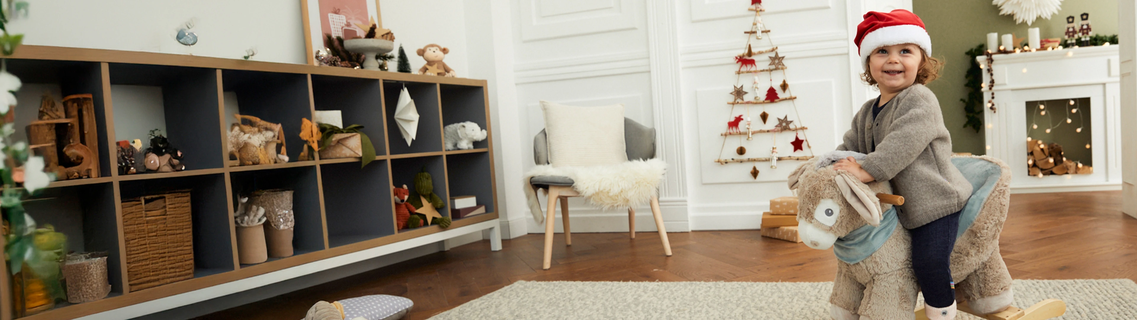 Ein Kind sitzt auf einem Schaukeltier Esel in einem Wohnzimmer, welches weihnachtlich dekoriert ist.