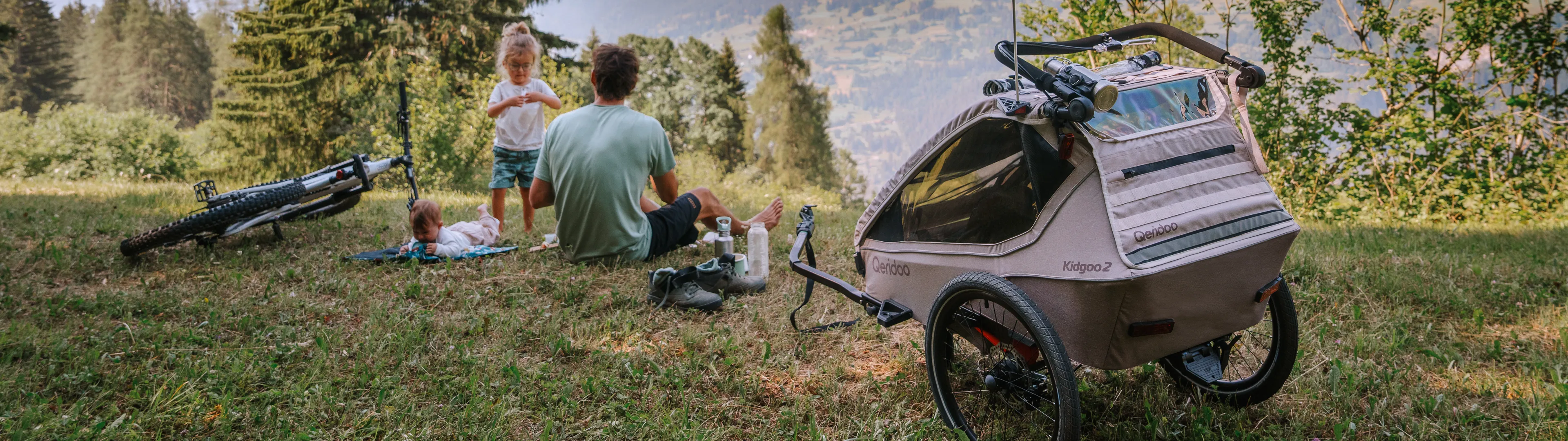 Eine Familie sitzt auf dem Berg; neben ihnen stehen ein Fahrrad und ein Fahrradanhänger.