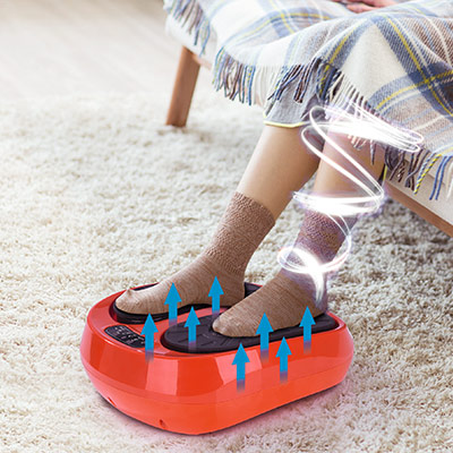 Person, die ein rotes Fußmassagegerät mit Vibration und nach oben zeigenden Pfeilen verwendet, die die Bewegung anzeigen. Gemütliche Einrichtung mit einer Decke in der Nähe.