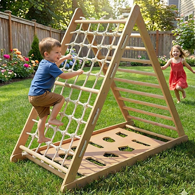 Ein kleiner Junge klettert in einem sonnigen Garten an einer Strickleiter auf ein hölzernes Spielgerüst, während sich ein Mädchen in einem roten Kleid lächelnd nähert.
