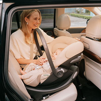 Eine Frau lächelt ein Baby in einem Kindersitz im Inneren eines Autos an. Der Sitz ist rückwärtsgerichtet, und der Innenraum ist hell und geräumig.