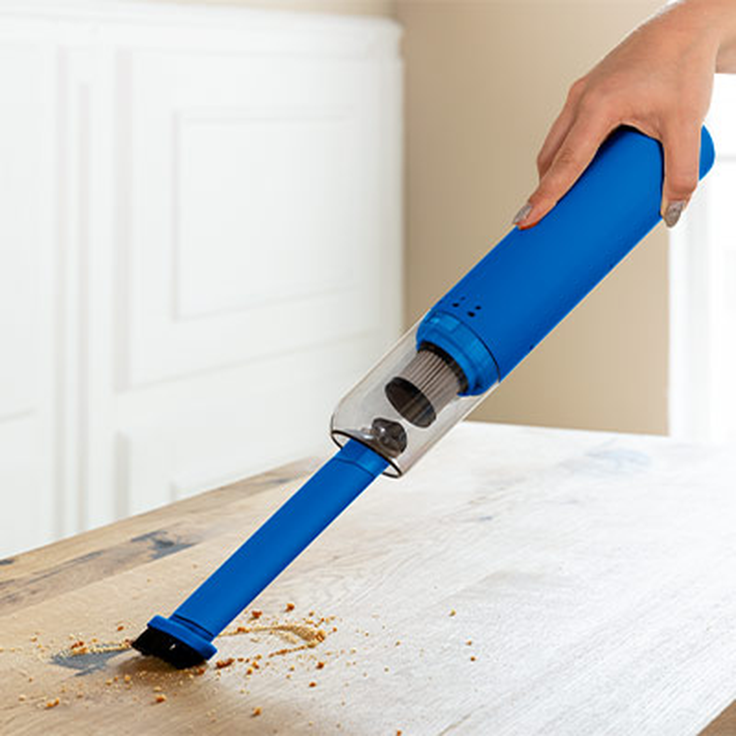 Eine Hand, die mit einem blauen Handstaubsauger Krümel von einem Holztisch entfernt.