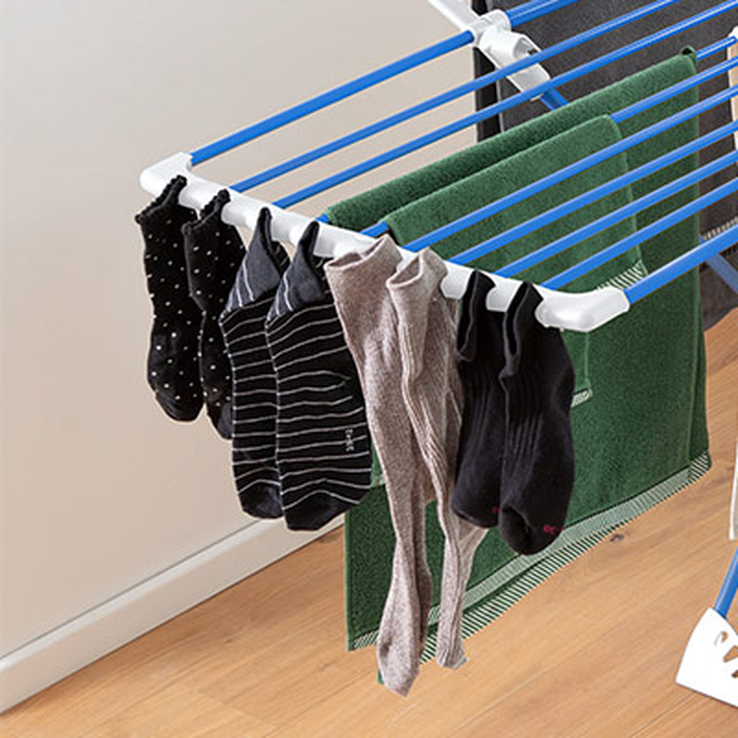 Socken und ein Handtuch trocknen auf einem Wäscheständer mit blauen Stangen, der auf einem Holzboden steht.
