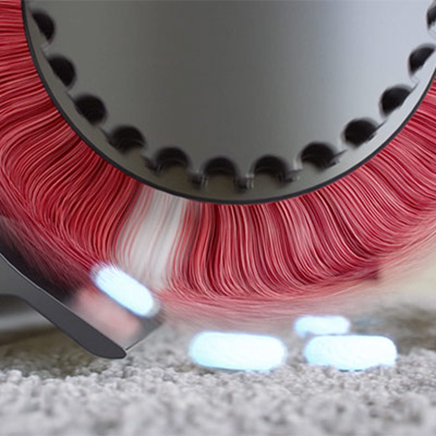 Nahaufnahme eines Staubsaugers mit einer Bürstenwalze mit roten Borsten, der einen Teppich reinigt und dabei kleine Partikel aufsaugt.