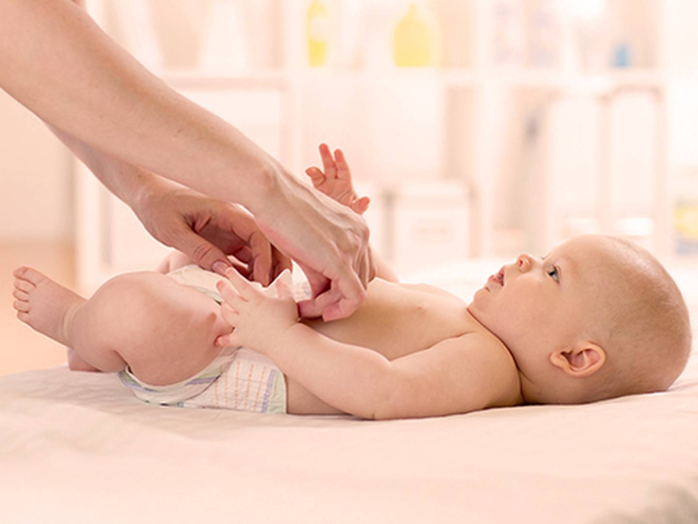 Das Baby liegt auf einer weichen Unterlage, während ein Erwachsener in einem gut beleuchteten Raum sanft die Windel wechselt.