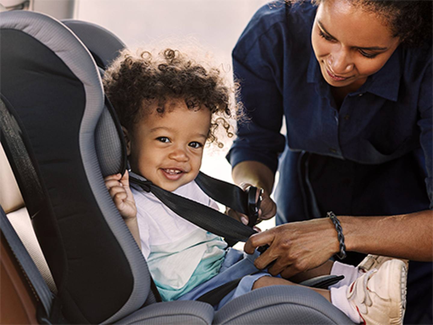 Eine Frau schnallt ein lächelndes Kleinkind in einem Auto in einen Kindersitz.