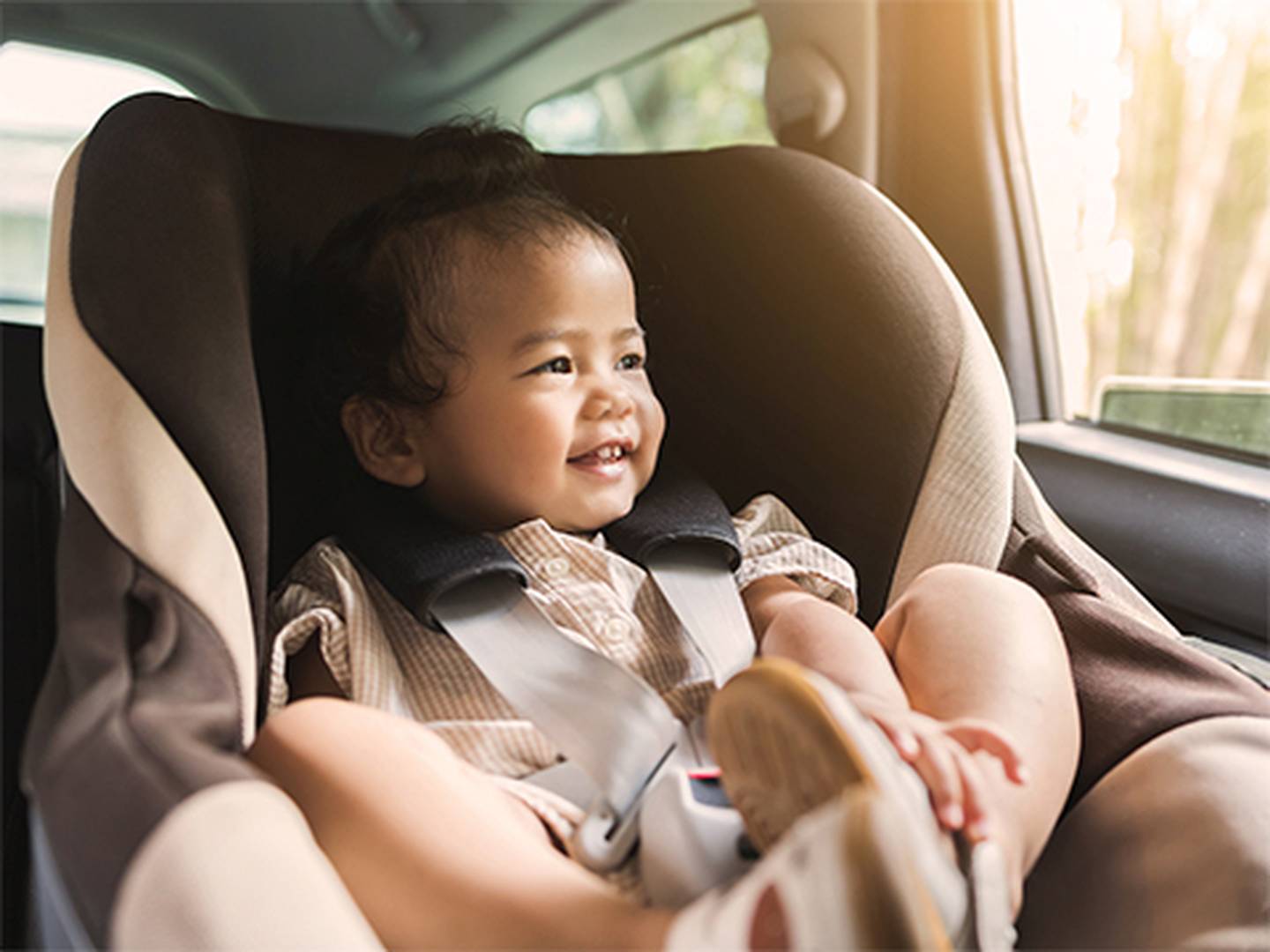 Ein lächelndes Baby sitzt in einem Autositz, gekleidet in ein gestreiftes Outfit, während Sonnenlicht durch das Autofenster strömt.