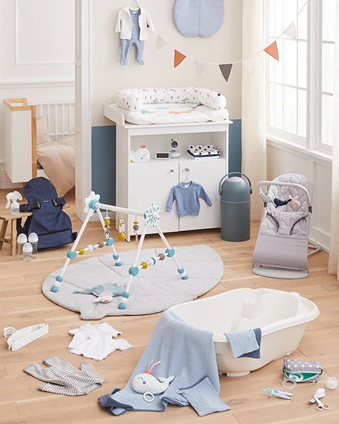 Ein gemütliches Kinderzimmer mit Babybett, Wickeltisch, Babywippe, Badewanne und Spielbogen. Maritime Dekoration mit Wandbildern und blauen Akzenten.