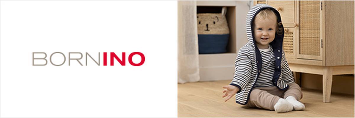 Ein Kleinkind in gestreiftem Kapuzenpullover und beiger Hose sitzt lächelnd auf einem Holzboden. Im Hintergrund sind ein Schrank und ein Korb zu sehen. Links steht „BORNINO“.