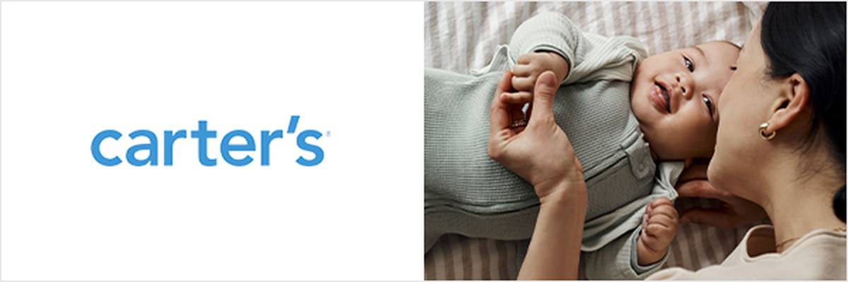 Ein lächelndes Baby in einem hellgrünen Outfit liegt auf einem Bett und hält die Hand einer Frau neben dem Carter's-Logo.