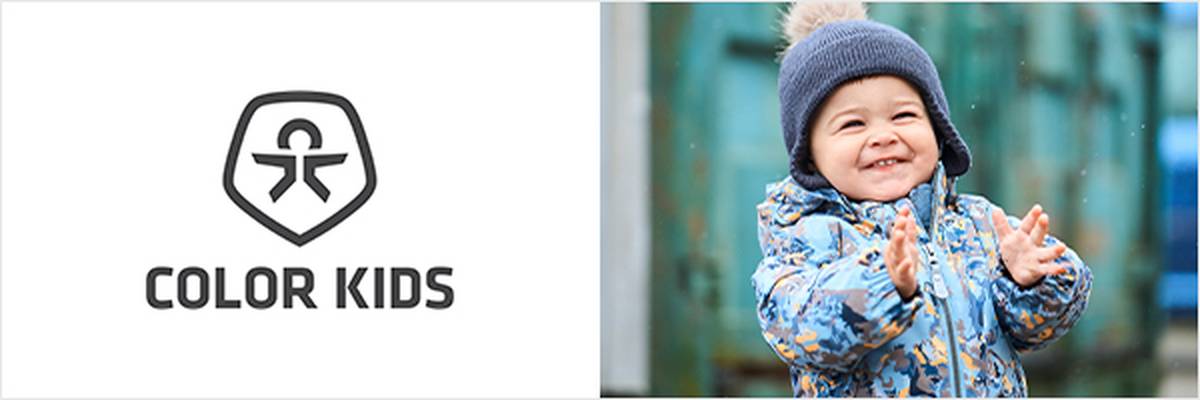 Ein Kleinkind in bunter Winterjacke, das klatscht und lächelt, links das „Color Kids“-Logo.