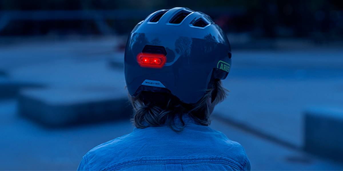 Eine Person mit Helm und rotem Rücklicht, von hinten gesehen, in einer schwach beleuchteten Umgebung im Freien.