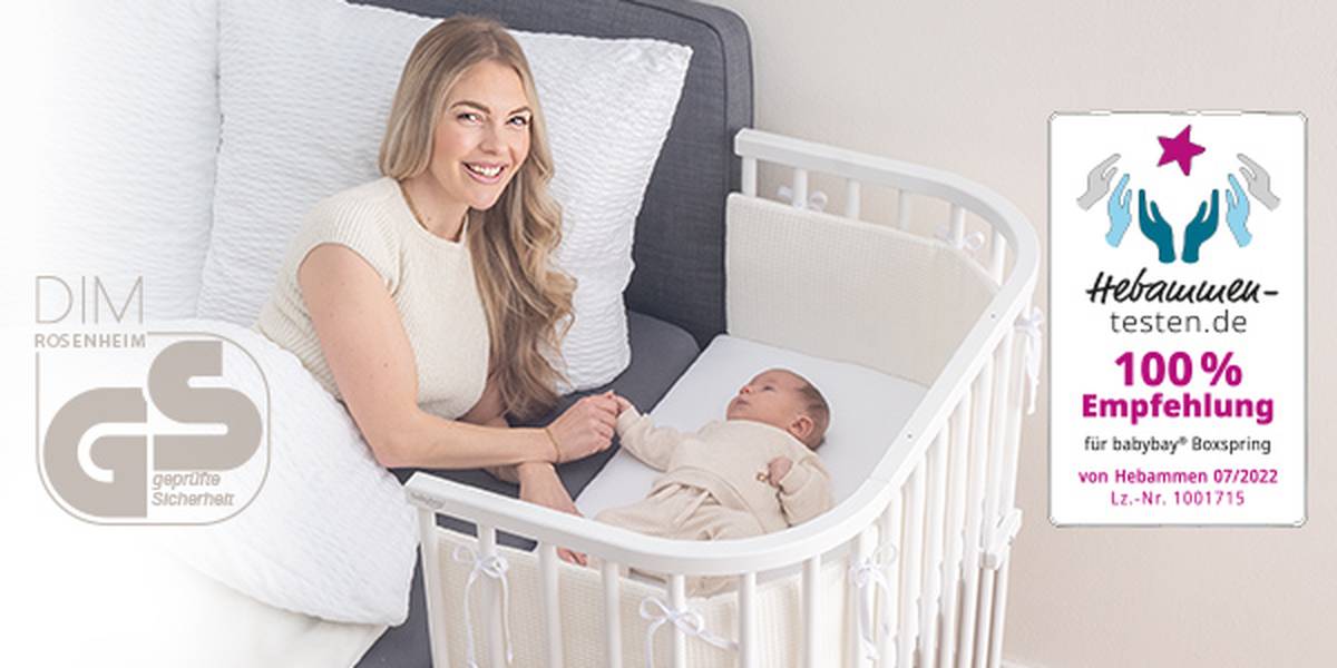 Eine Frau lächelt ein Baby an, das in einem weißen Gitterbett liegt. Auf der rechten Seite sind ein Zertifizierungslogo und ein Empfehlungstext zu sehen.