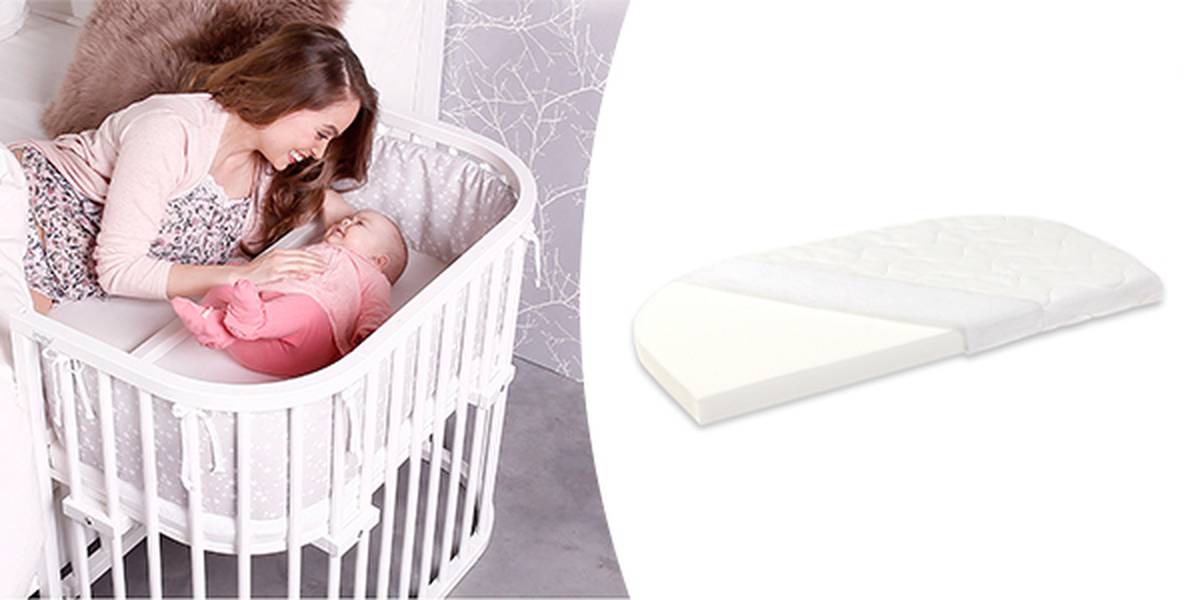 Eine Mutter lächelt ihr Baby in einem weißen ovalen Kinderbett an. Daneben ist das Bild einer weißen Kinderbettmatratze zu sehen.