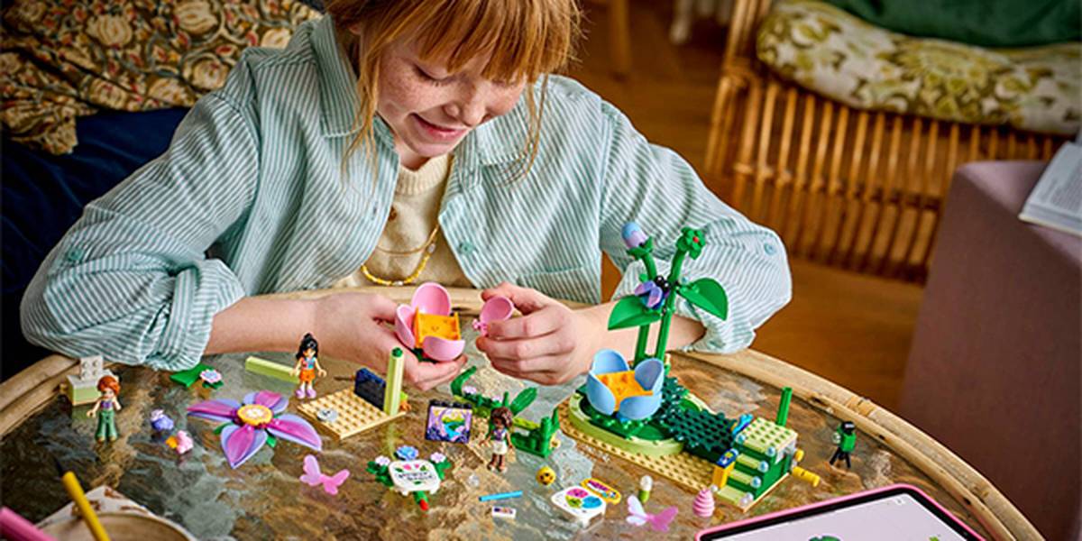 Ein Kind spielt auf einem Tisch mit bunten LEGO-Spielzeugen und konzentriert sich dabei auf ein Set zum Thema Garten mit Pflanzen und Figuren.