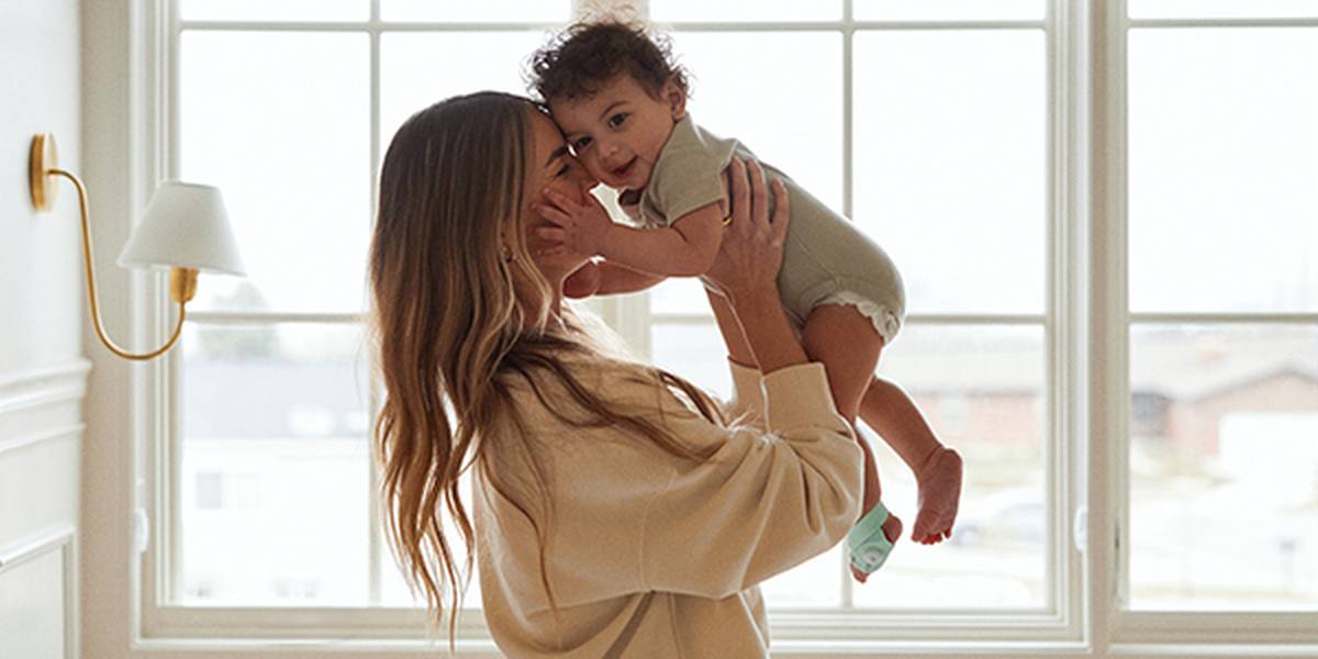 Eine Frau hält ein lächelndes Baby in der Nähe eines großen Fensters und schafft so eine warme und fröhliche Szene im Inneren.