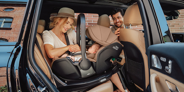 Ein lächelndes Paar setzt ein Baby in einem geparkten Auto in einen rückwärtsgerichteten Kindersitz – mit Fokus auf Sicherheit und Komfort.