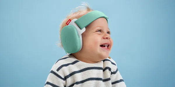 Ein lächelndes Baby mit blonden Haaren, das grüne Ohrenschützer und einen gestreiften Pullover trägt, vor blauem Hintergrund.