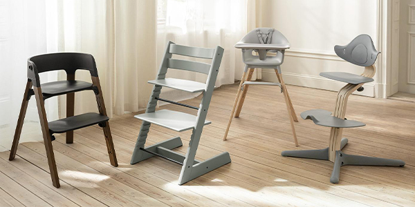 Vier moderne Hochstühle in verschiedenen Stilen und Farben auf einem Holzboden in einem hellen Raum.