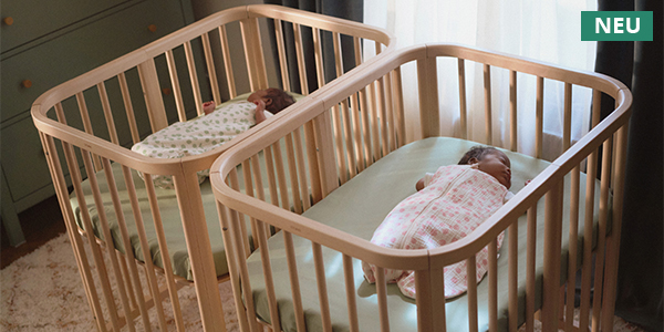 Zwei Stokke Sleepi Mini Beistellbetten aus hellem Holz mit schlafenden Babys in einem gemütlichen Schlafzimmer. Hinweis „NEU“ oben rechts.