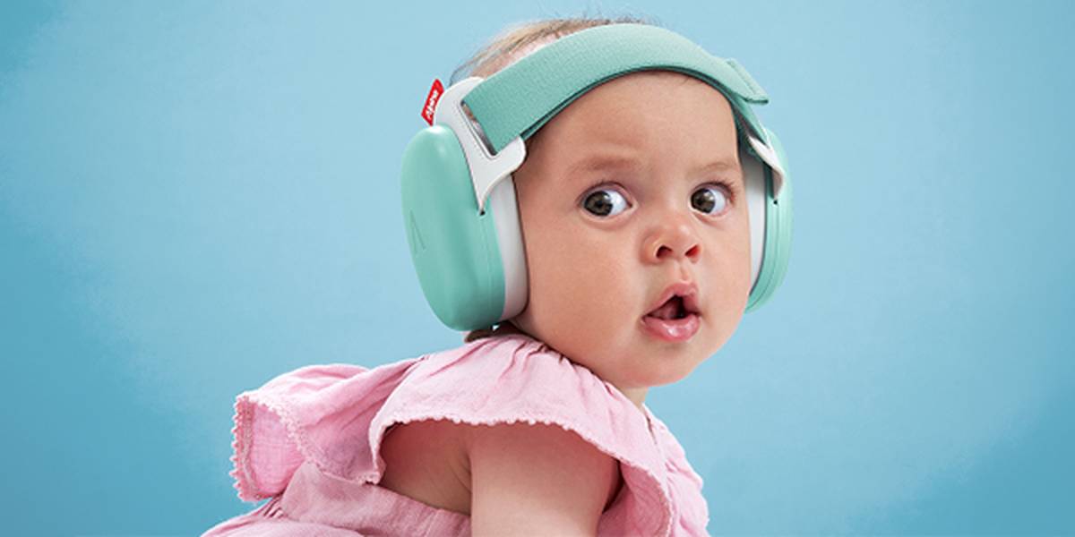 Ein Baby in einem rosa Outfit, das mintgrüne Kopfhörer mit Geräuschunterdrückung trägt und vor einem blauen Hintergrund überrascht dreinschaut.