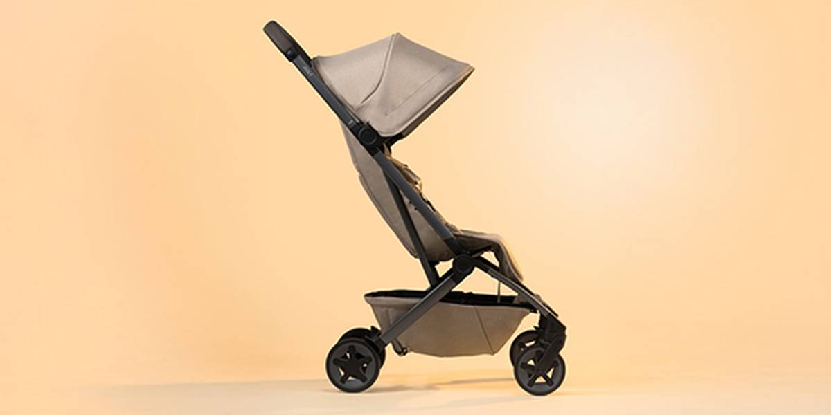 Seitenansicht eines modernen beigen Kinderwagens mit Verdeck vor hellorangefarbenem Hintergrund.