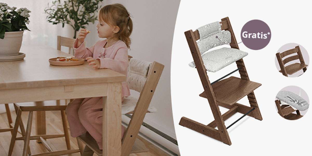 Ein Kind in einem rosa Outfit sitzt auf einem Stokke Tripp Trapp Hochstuhl und isst. Hinweis auf Gratis Sitzkissen