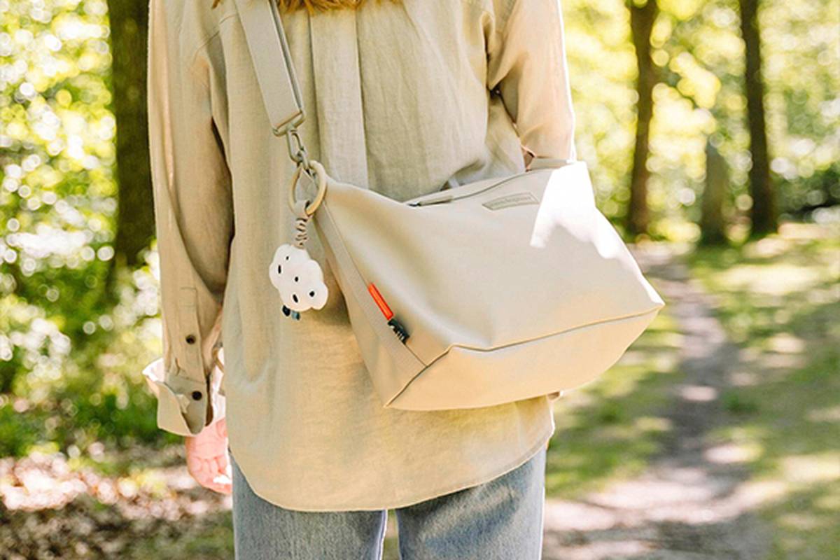 Person, die auf einem Waldweg geht, ein beiges Hemd und Jeans trägt und eine beige Wickeltasche mit einem süßen Wolkenschlüsselanhänger trägt.