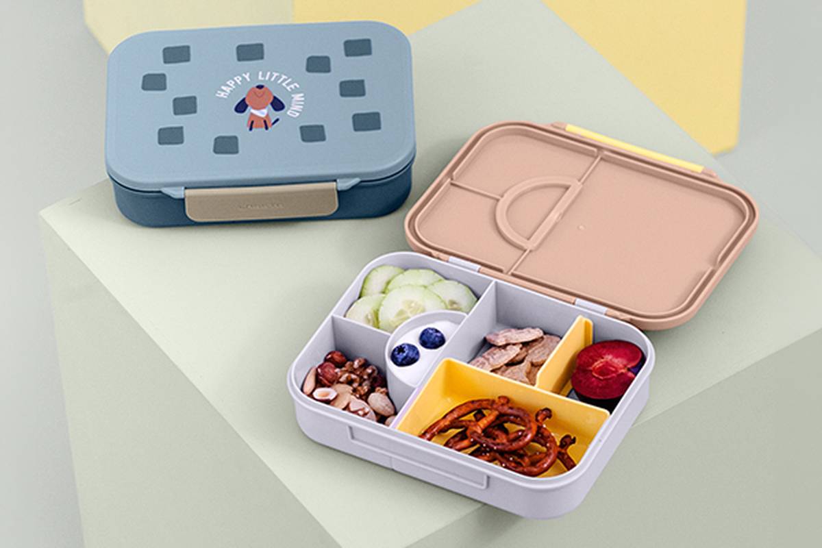 Offene Lunchbox mit Gurke, Blaubeeren, Nüssen, Trockenfrüchten und Brezeln; geschlossene Box daneben.