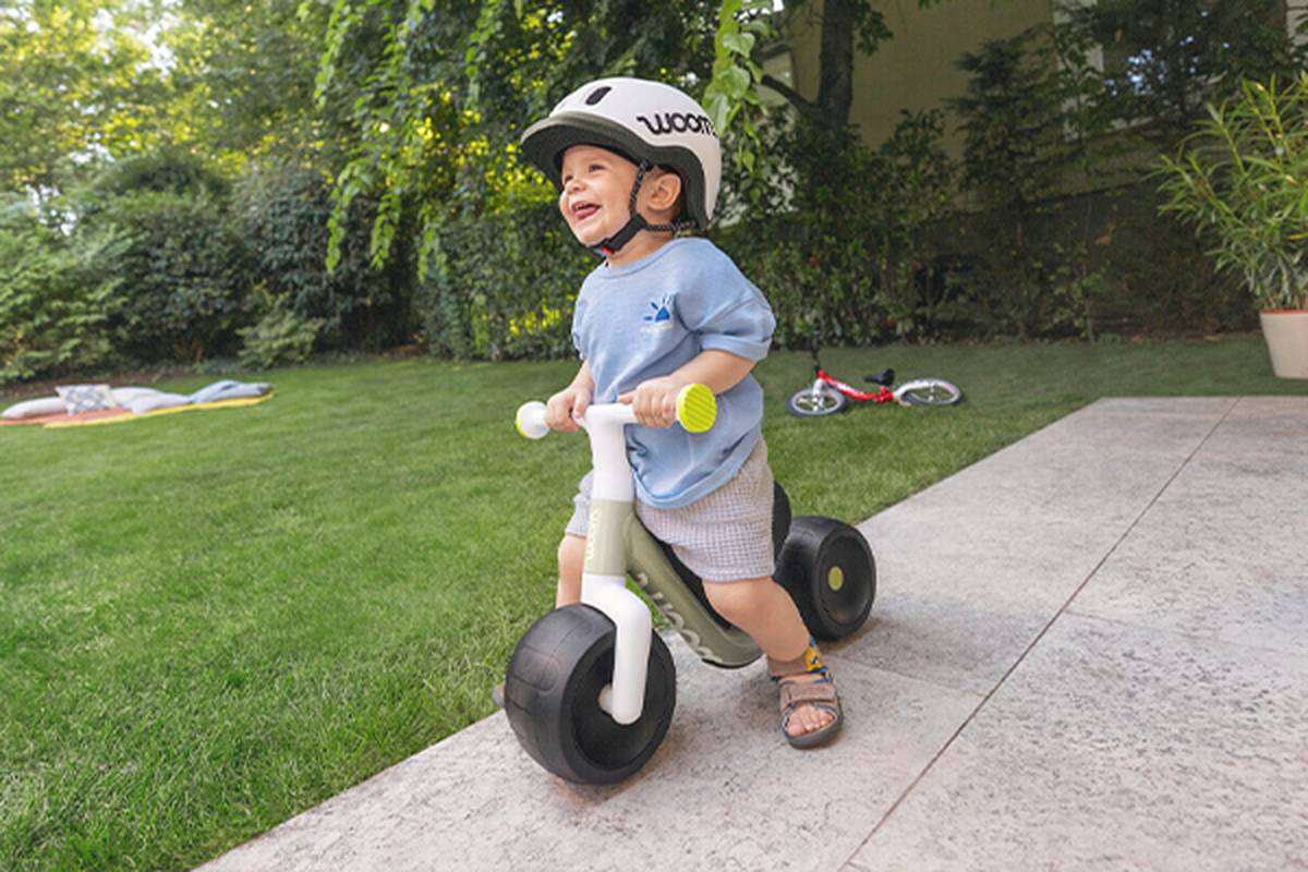 A child wearing a helmet is smiling while riding a bike by the seaside on a sunny day.
