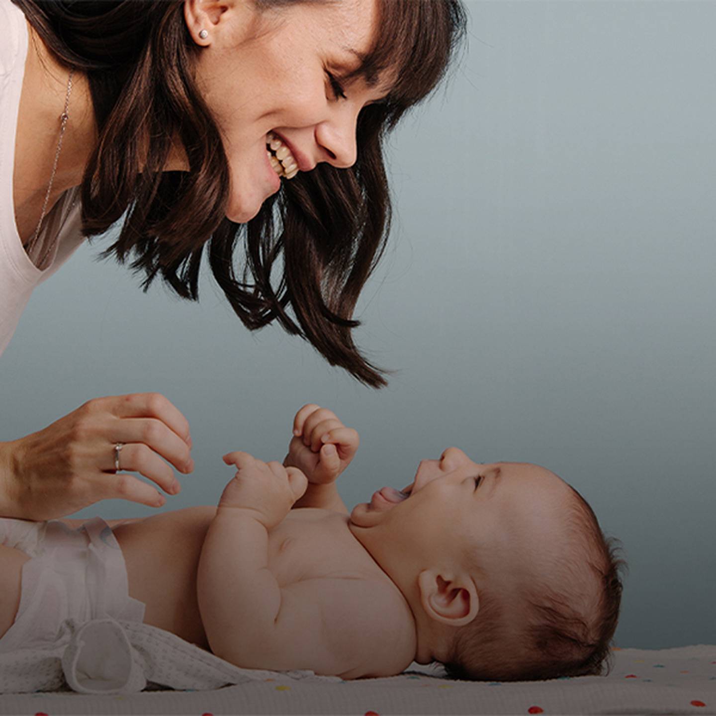 Eine Frau lächelt ein lachendes Baby an, das auf einem Wickeltisch liegt.