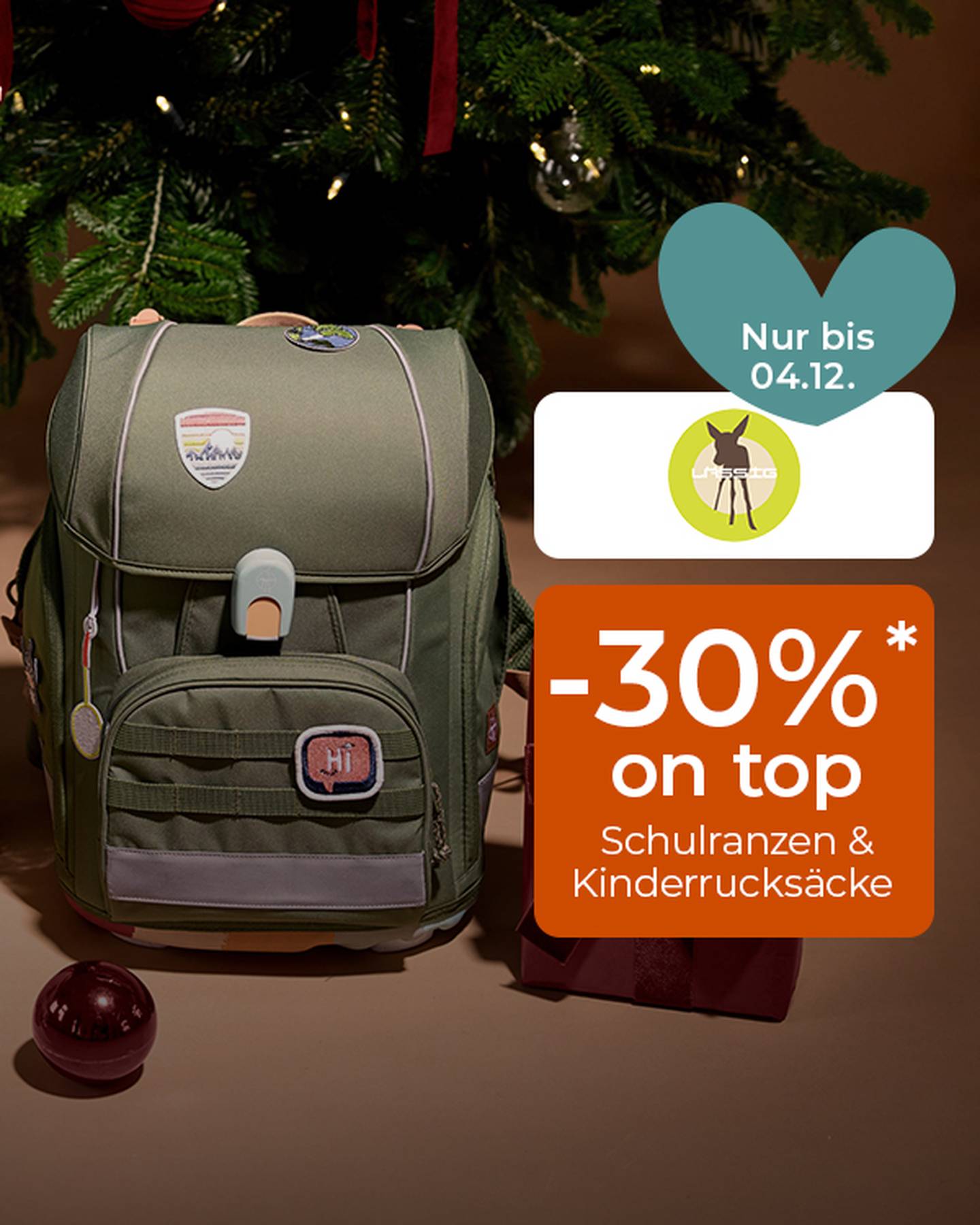 Ein grüner Kinderschulrucksack unter einem geschmückten Weihnachtsbaum, daneben ein orangefarbenes Preisschild mit der Aufschrift „-30%“: Schulranzen & Kinderrucksäcke