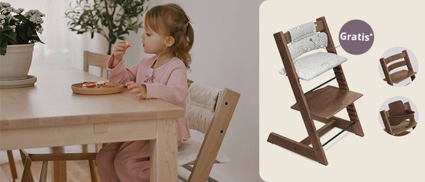 Ein Kind in einem rosa Outfit sitzt auf einem Stokke Tripp Trapp Hochstuhl und isst. Hinweis auf Gratis Sitzkissen